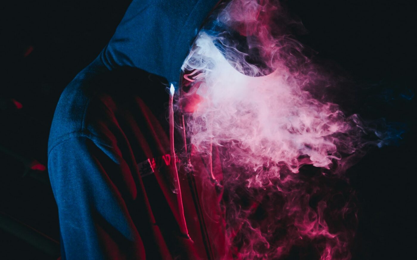 Figure in a hoodie surrounded by coloured vapour
