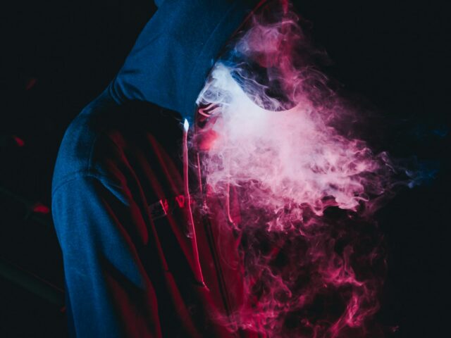Figure in a hoodie surrounded by coloured vapour